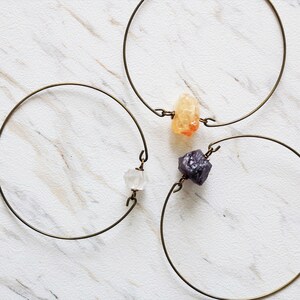 May include: Three gold wire bracelets with different colored crystal charms. The charms are a clear crystal, a light orange crystal, and a dark purple crystal.