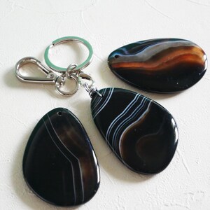 May include: Three black agate stone keychains with white and brown stripes. Each stone is attached to a silver key ring.