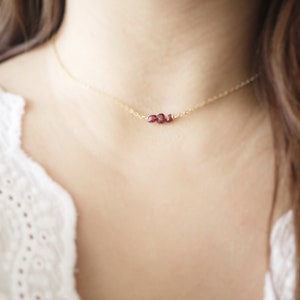 May include: A delicate gold chain necklace with a small cluster of red garnet stones.