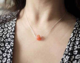 May include: A silver chain necklace with a single, small, orange gemstone pendant.
