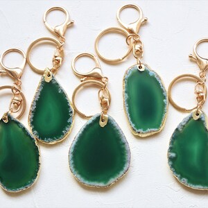 May include: Five green agate slice keychains with gold-toned metal rings and clasps. The agate slices are all different shapes and sizes, but they all have a similar green and white color scheme.