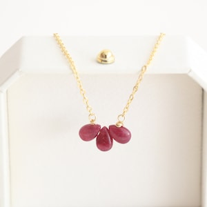 May include: A gold chain necklace with three teardrop-shaped ruby red stones.