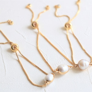 May include: Three gold chain bracelets with a pearl charm on each. The bracelets have a sliding clasp to adjust the fit.