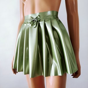 May include: A light green, pleated skirt with a bow detail at the waist. The skirt has a shiny, satin-like finish and a flared silhouette. The "Charm Latex" logo is visible at the bottom.