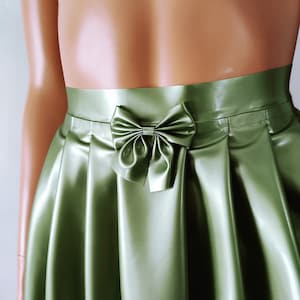May include: A green satin skirt with a bow detail at the waist. The skirt has a pleated design and a shiny finish. The logo "Charm Latex" is visible at the bottom right.