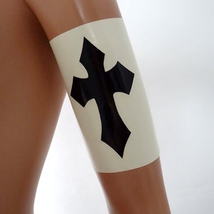 Peut inclure: Un brassard en latex blanc avec un motif de croix noire. Le brassard est porté sur le bras d'un mannequin.