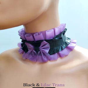 May include: A black and lilac latex choker with a ruffled design. The choker features a black band with a lilac bow and matching lilac ruffles. The text "Black & Lilac Trans" and "Charm Latex" is visible.