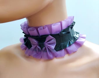 May include: A black and lilac latex choker with a ruffled design. The choker features a black band with a lilac bow and matching lilac ruffles. The text "Black & Lilac Trans" and "Charm Latex" is visible.