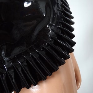 May include: A black latex skirt with a ruffled hem. The glossy material reflects light, highlighting the skirt's texture and design. The "Charm Latex" logo is visible at the bottom.