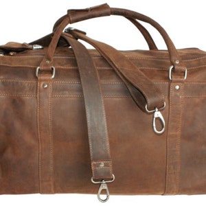 May include: A brown leather duffel bag with a long shoulder strap and two top handles. The bag has a zipper closure and a silver metal hook on the strap.