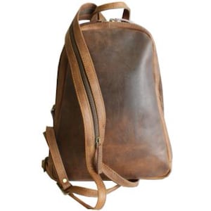 Puede incluir: Una mochila de cuero marrón con cierre de cremallera y correas ajustables. La mochila tiene un aspecto desgastado y está hecha de cuero de alta calidad.
