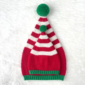 May include: Two red and white striped knit elf hats with green pom-poms. The smaller hat is inside the larger hat.