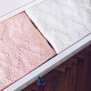 May include: A white drawer with a pink and white knitted blanket inside. The drawer is open and the blanket is folded in half.