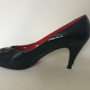 May include: Black peep-toe high heel pump with a red lining and a geometric design on the toe.