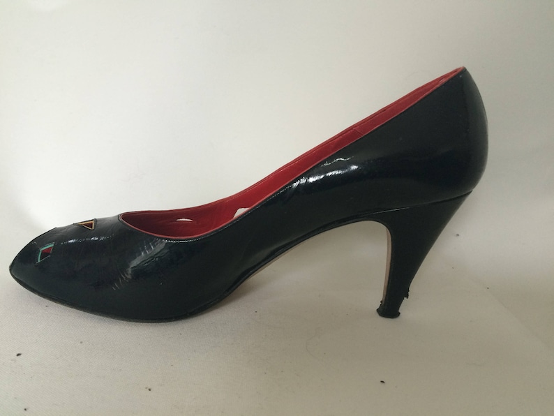 May include: Black peep-toe high heel pump with a red lining and a geometric design on the toe.