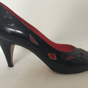May include: Black high-heeled pumps with red and gold accents. The shoes have a peep-toe design and a stiletto heel.