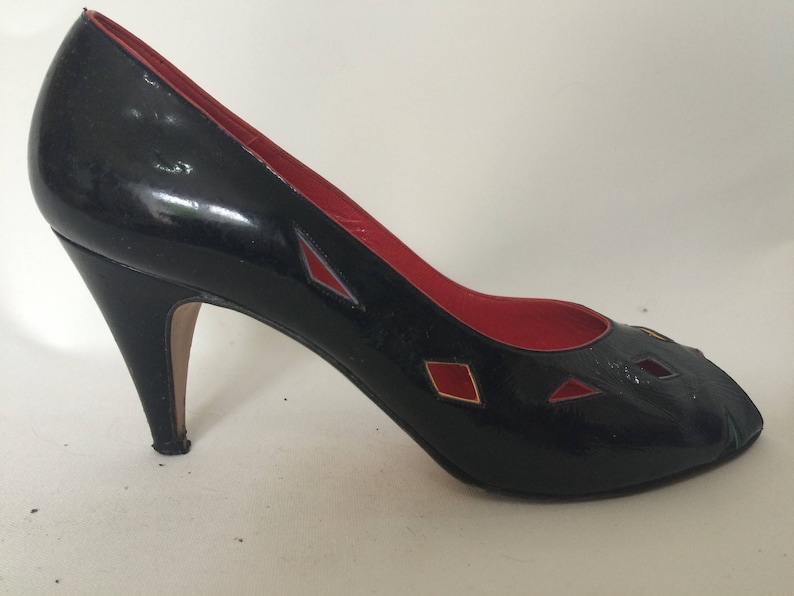 May include: Black high-heeled pumps with red and gold accents. The shoes have a peep-toe design and a stiletto heel.