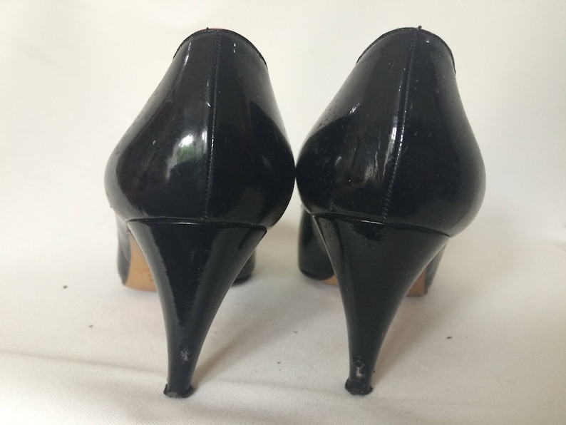 May include: A pair of black patent leather high heel pumps with stiletto heels.