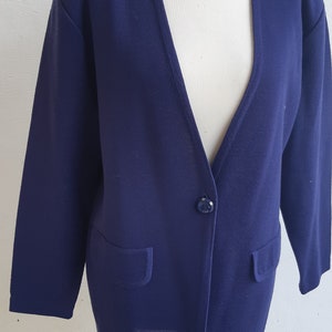 May include: A navy blue cardigan with a single button closure and two pockets. The cardigan is on a wooden mannequin.