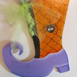 May include: Purple witch's boot with a black and orange spiderweb design and a green tulle bow. The boot is decorated with glitter.