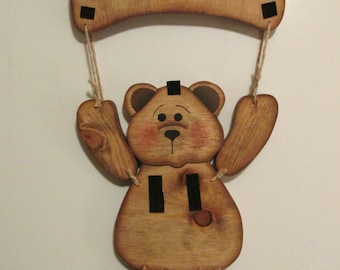 May include: Wooden welcome sign with a brown bear holding the sign. The sign is painted with the word "WELCOME" in white letters.