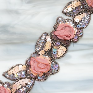 May include: A beaded trim featuring pink fabric roses and iridescent sequins. The trim is ideal for adding a touch of elegance to any project.