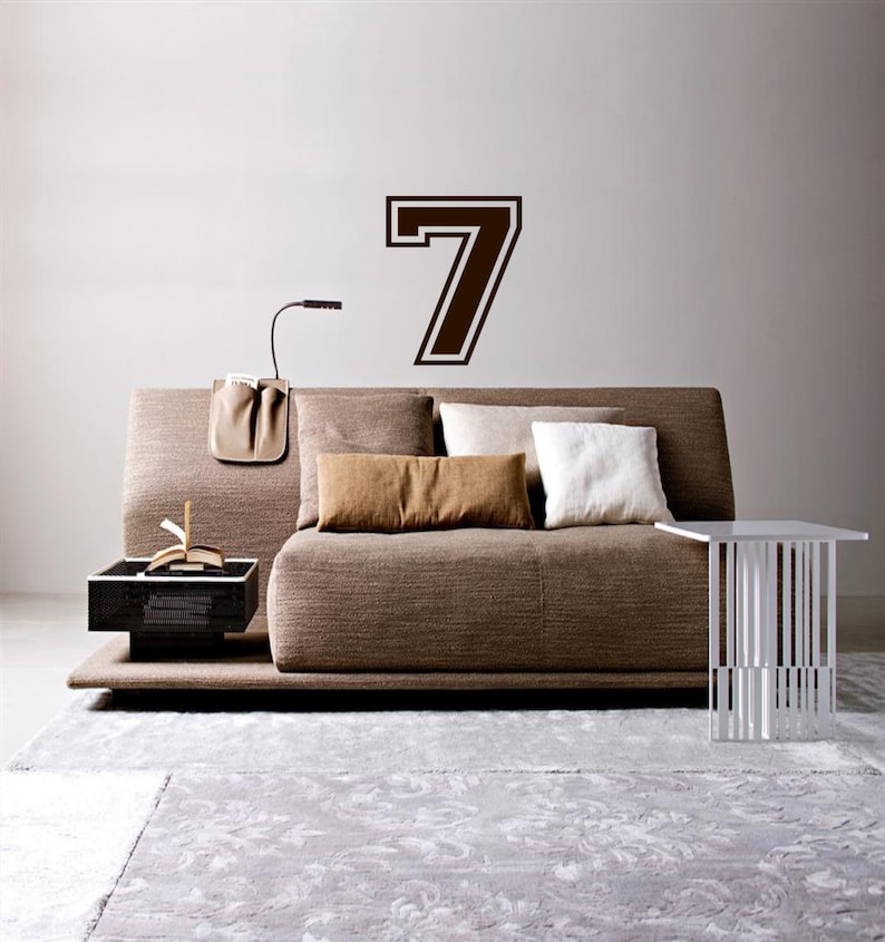 May include: A brown couch with pillows and a side table in a living room. A large brown number seven is on the wall behind the couch.