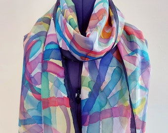 May include: A colorful silk scarf with a geometric pattern of overlapping circles and lines in shades of pink, blue, green, yellow, and orange. The scarf has a black trim.