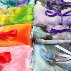 May include: A stack of colorful silk scarves with different patterns and tied with ribbons. The scarves are arranged in a rainbow order, with red, orange, yellow, green, blue, and purple.
