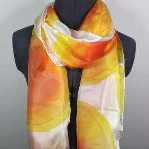 May include: A white silk scarf with a hand-painted design of orange and yellow watercolor circles.