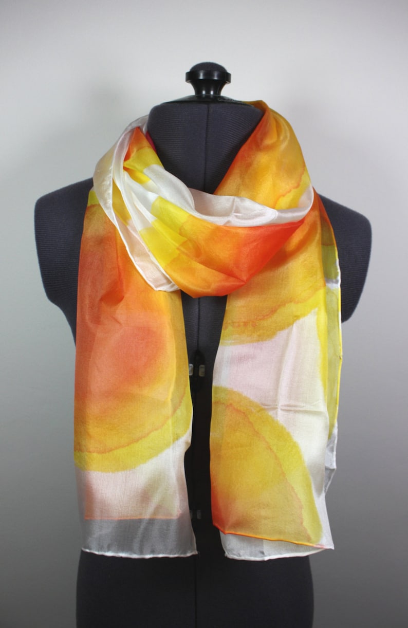 May include: A white silk scarf with a hand-painted design of orange and yellow watercolor circles.