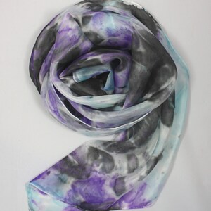 May include: A white silk scarf with a tie-dye pattern in shades of purple, blue, and black.