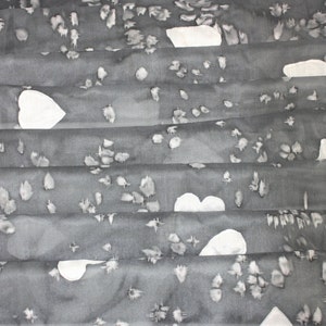 Peut inclure: Une &eacute;charpe en soie grise avec un motif de c&oelig;urs blancs. L'&eacute;charpe est pli&eacute;e en plusieurs couches, cr&eacute;ant un aspect textur&eacute;.