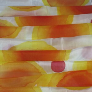 May include: A white silk scarf with a hand-painted design of overlapping orange, yellow, and pink circles.