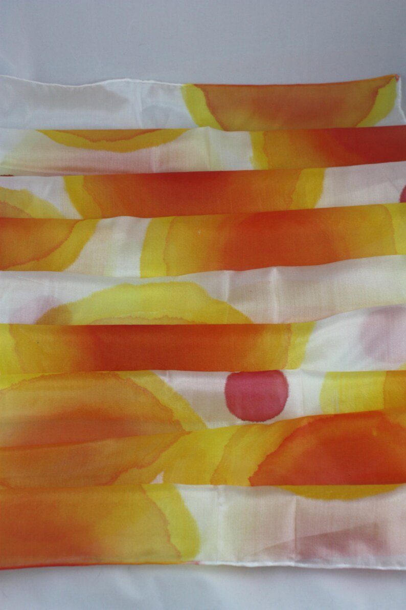 May include: A white silk scarf with a hand-painted design of overlapping orange, yellow, and pink circles.