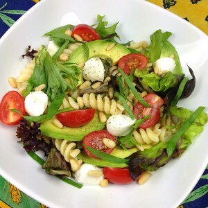 May include: A white bowl filled with a salad of pasta, avocado, mozzarella cheese, cherry tomatoes, and fresh herbs.