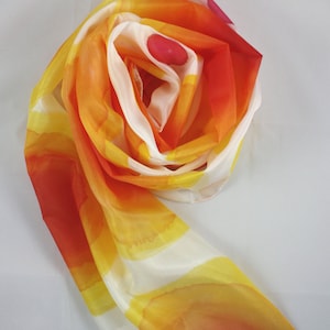 May include: A white silk scarf with orange, yellow, and red watercolor-like designs. The scarf is folded and tied into a loose knot.