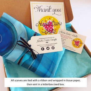 May include: A blue and white silk scarf with a gold ribbon tied around it. The scarf is packaged in a box with tissue paper and a thank you card that says "Nicola Davis Crafts".