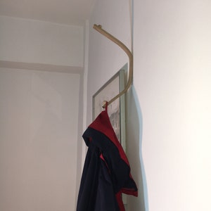 May include: A wooden coat hook mounted on a white wall with a black and red jacket hanging from it.