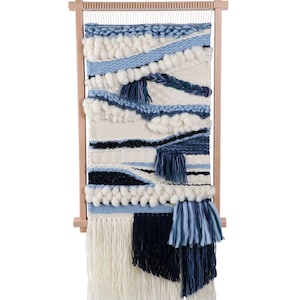 May include: A blue and white woven wall hanging with fringe on a wooden loom. The hanging features a variety of textures and patterns, including stripes, waves, and pom-poms.