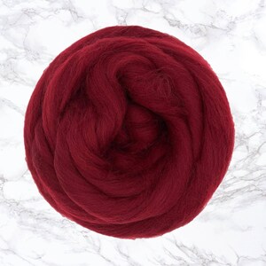 Op de afbeelding: Een bol dieprode merinowol, ideaal voor fiber art projecten. De wol is dicht opeengepakt en ziet er zacht uit, met een licht getextureerd oppervlak. De achtergrond is een wit marmerpatroon.