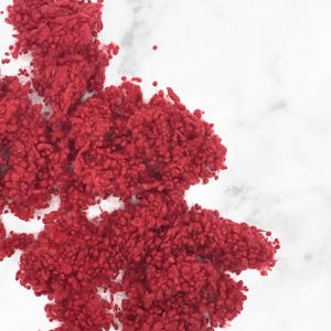 Può includere: Un mucchio di fibre di filato rosso su una superficie di marmo bianco.