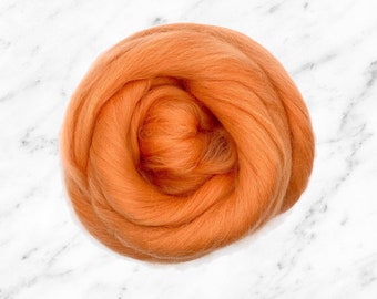 May include: A close-up of a ball of orange wool roving. The wool is soft and fluffy, and it is perfect for felting or spinning.