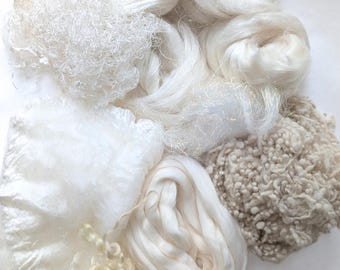 May include: A collection of various white and off-white textile fibers, including smooth silk-like roving, curly wool locks, textured bouclé yarn, and fine, wispy synthetic filaments arranged in a cluster of different textures and densities.
