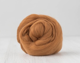 Op de afbeelding: Een bol bruine wolvlies, strak gewikkeld en getextureerd. De wol heeft een warme, aardse tint en ligt op een wit houten oppervlak. Ideaal voor textielkunstprojecten zoals naaldvilten of natvilten.