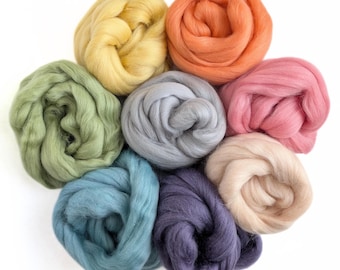 May include: A collection of colorful wool roving in shades of yellow, orange, pink, green, blue, gray, and purple. The wool is arranged in a circular pattern, with each color forming a separate, rounded bundle. The background is plain white.