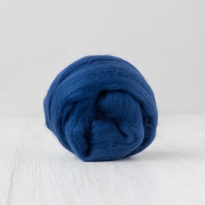 May include: A ball of deep blue wool roving, tightly wound and textured. The wool is a rich, saturated colour, and appears soft and fluffy. The background is a light, neutral colour, highlighting the vibrant blue of the wool.