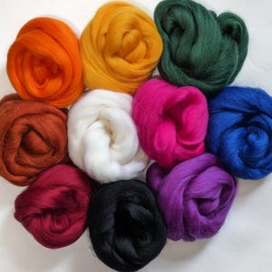 May include: A collection of colorful wool roving in various shades, including orange, yellow, green, pink, blue, purple, red, white, brown, and black. The wool is arranged in fluffy, coiled bundles, ideal for fiber art projects like felting and spinning.
