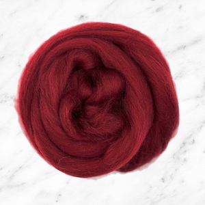 Puede incluir: Primer plano de una bola de fibra de lana de color rojo oscuro. La lana es suave y esponjosa, perfecta para el fieltro o el hilado.