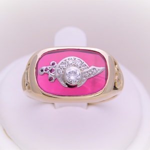 May include: A gold ring with a pink stone set in a rectangular bezel. The stone has a white diamond and smaller diamonds set in a crescent moon design.